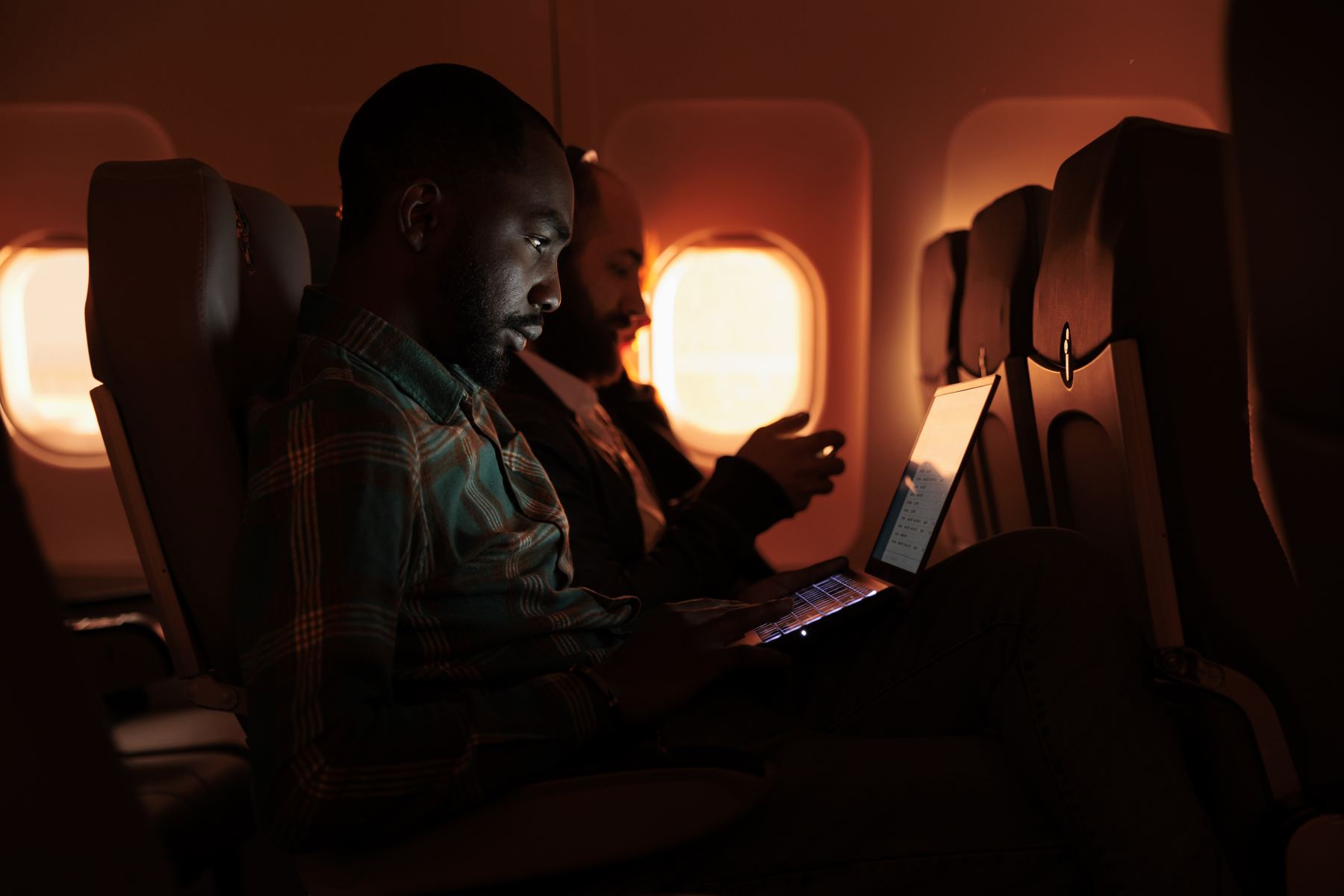 Man working on a laptop on a plane at sunset